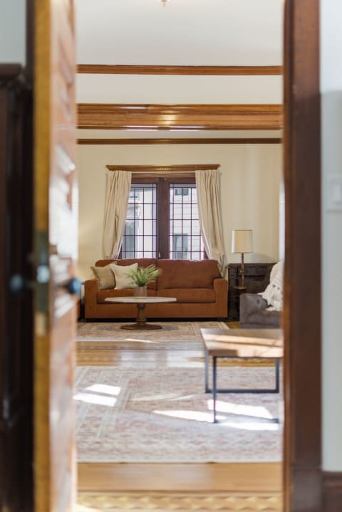 Cozy living room with brown sofa, wooden beams, and natural light from windows.
