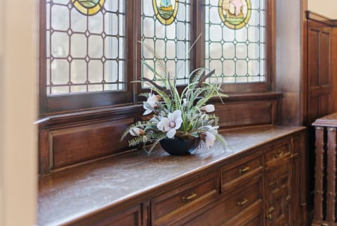 Wooden cabinet with stained glass windows and a floral arrangement on top.