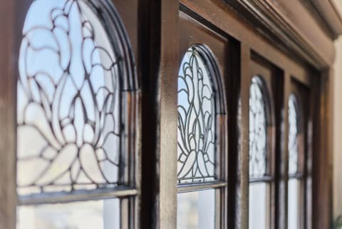 Close-up of stained glass window details in a wooden frame, featuring delicate floral patterns and a polished finish.