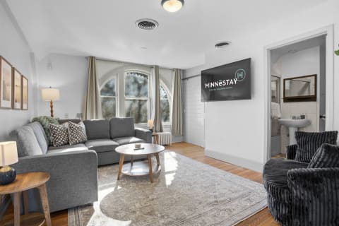 Stylish living room featuring a grey sectional sofa, plush round chair, and arched windows with curtains.