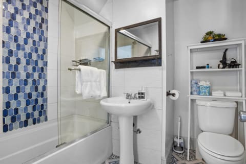 Stylish bathroom with blue hexagonal tiles, glass shower, and organized storage shelves.