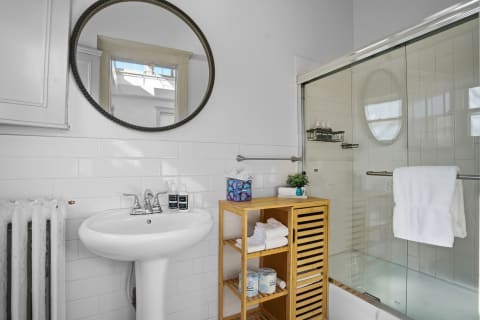 Modern bathroom featuring a pedestal sink, wooden storage, and a glass shower.