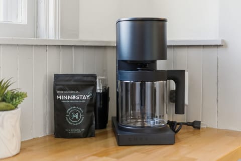 A contemporary coffee station featuring a black coffee maker and a bag of MINNESTAY coffee beans next to a small succulent plant.