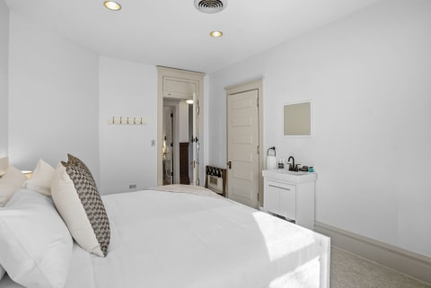 A serene bedroom with crisp white linens, a decorative pillow, and a convenient in-room sink.