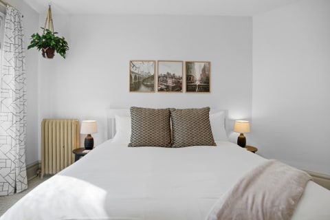 A cozy bedroom featuring a white bed, decorative pillows, bedside lamps, and urban-themed wall art.