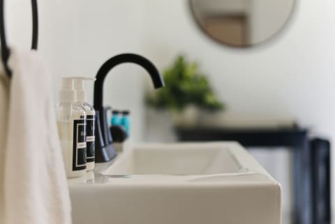 Modern bathroom sink with black faucet, clear soap and lotion bottles, and a white towel.