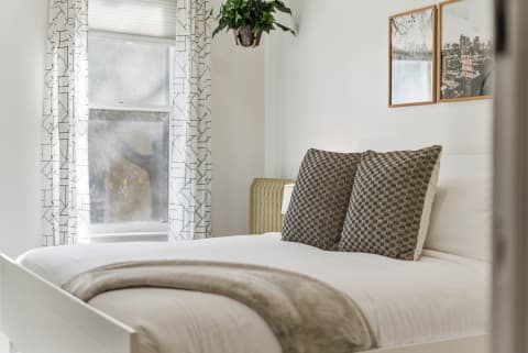 A serene bedroom with white linens, geometric curtains, and framed urban photographs.