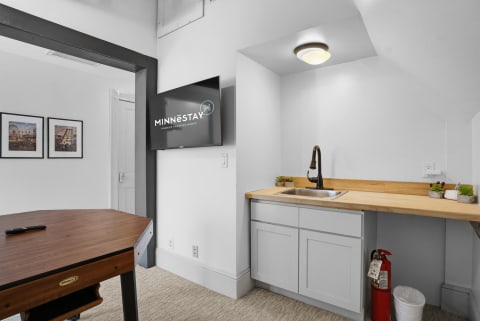 A cozy game room with a kitchenette, showcasing a sink and counter space, framed pictures on the wall, and a wall-mounted TV.