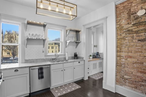 A gourmet kitchen showcasing granite counters, exposed brick walls, and a modern light fixture.