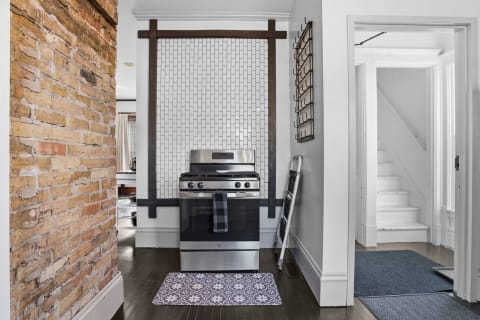 A modern kitchen with a stainless steel gas range, exposed brick wall, and herringbone tile backsplash.