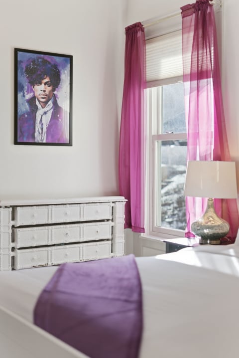 A stylish bedroom with purple curtains, a white dresser, and an artistic portrait on the wall.