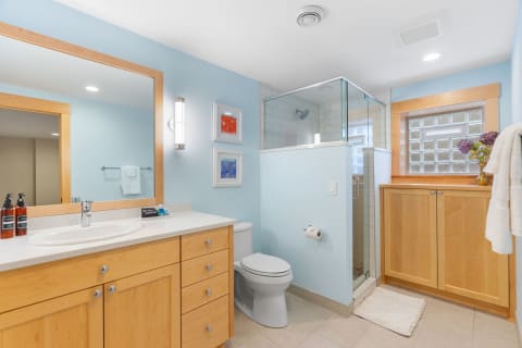 Modern bathroom with light blue walls, wooden cabinetry, and glass shower.