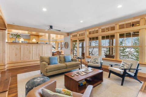 Cozy living room with a beige sofa, black armchairs, and large windows overlooking greenery.