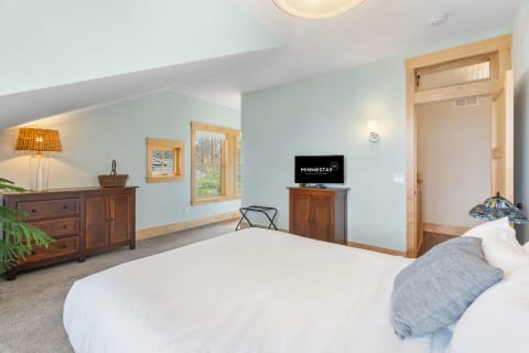 Cozy bedroom with a sloped ceiling, wooden furniture, and natural light from windows.