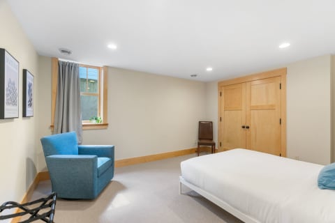 Minimalist bedroom featuring a bed, blue armchair, and natural light from the window.