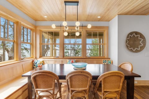 Bright dining area with wooden furniture and large windows overlooking trees.