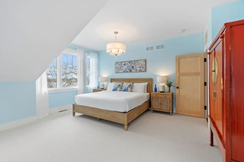 A serene bedroom featuring a wooden bed, light blue walls, and bright white curtains.