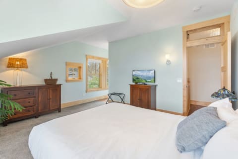 Interior view of a serene bedroom with a bed, dresser, lamp, and TV.