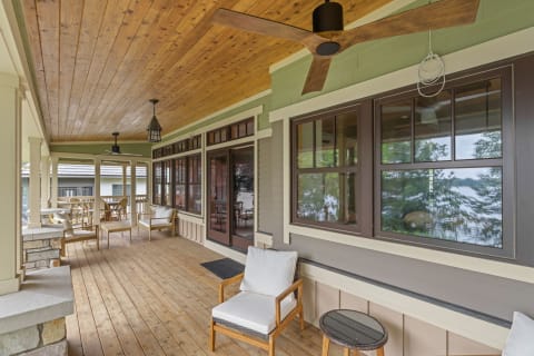 A cozy porch featuring wooden flooring, stylish chairs, and large windows with lovely views.