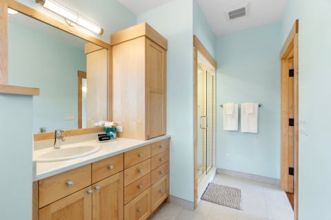 Contemporary bathroom with light wood vanity, blue walls, and a glass-enclosed shower.