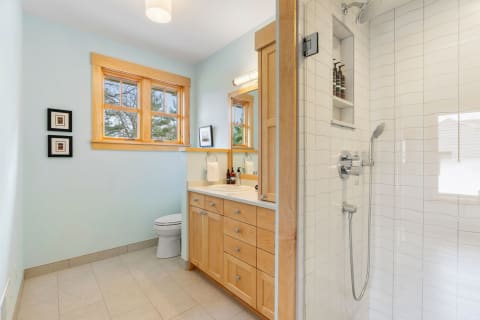 A modern bathroom featuring a light blue wall, wooden cabinetry, and a stylish shower.