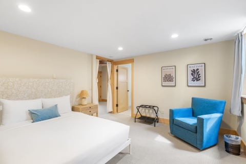 Cozy bedroom with a white bed, blue accent chair, and artwork on the walls.