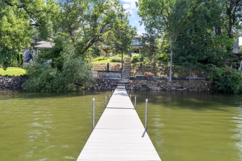 Wooden dock extending into calm lake waters with houses and trees in the background.