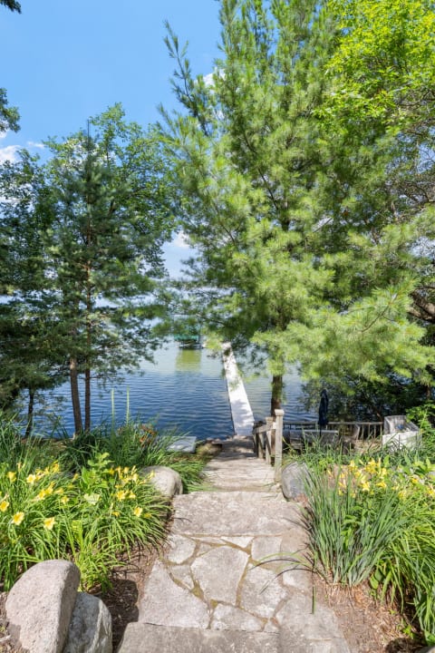 Stone pathway bordered by flowers leading to a lake.
