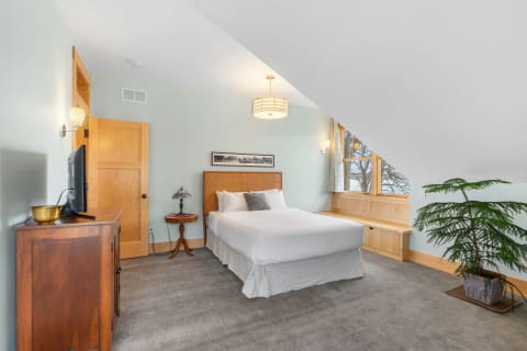 Modern bedroom with a queen bed, wooden accents, and large windows.