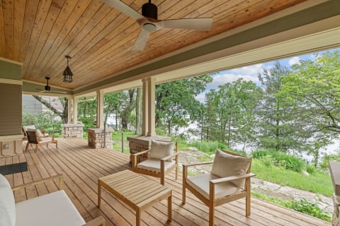 A wooden porch with comfortable seating overlooking trees and a water body.