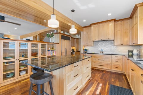 Spacious kitchen with light wood cabinets, dark granite island, and wooden flooring.