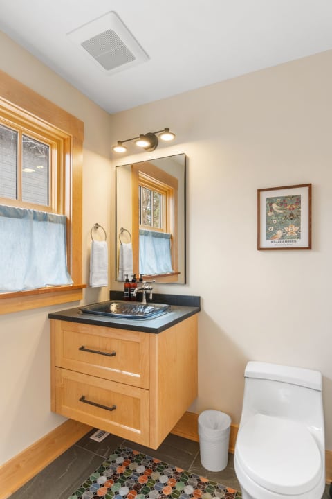 Small bathroom with light wood accents, modern sink, and colorful tile flooring.