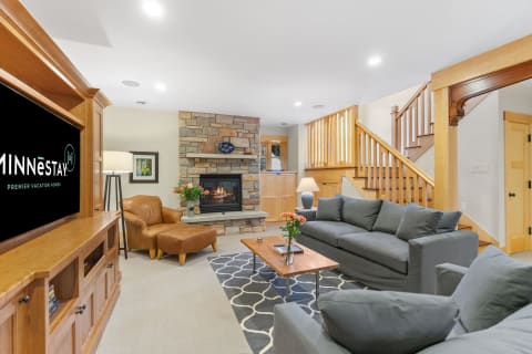 Cozy living room with a grey sectional sofa, wooden coffee table, stone fireplace, and a leather armchair.