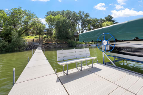 Lakeside dock with a bench and a covered boat, surrounded by trees.