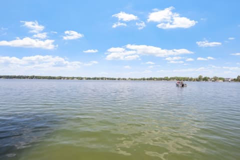 A scenic view of a lake with a small boat and white clouds in the sky.