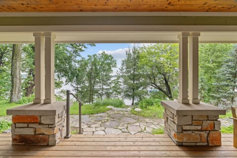 View from a covered porch featuring stone columns and a pathway leading to the water.