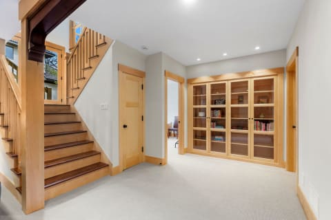 Modern entryway featuring wooden stairs and a glass-fronted bookshelf.