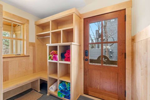 A wooden entryway with cubbies filled with colorful towels and a glass-paneled door.