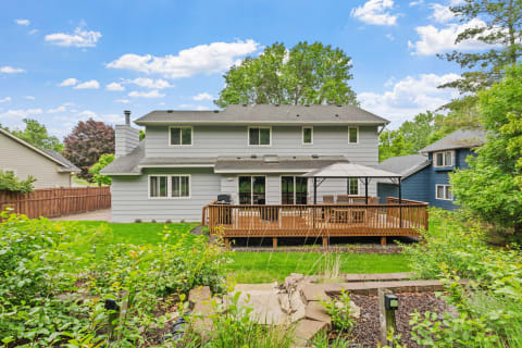 Back view of a two-story gray house with a wooden deck and gazebo surrounded by greenery.