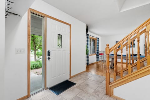 Entrance hallway of a home featuring a white door, tiled floor, and wooden staircase.