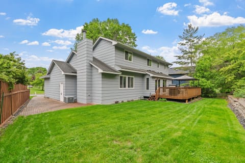 Exterior view of a modern gray house with a wooden deck and green lawn.