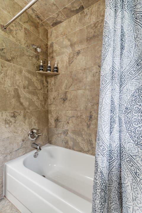 A stylish bathroom with marbled tile walls and a white bathtub, accompanied by a patterned shower curtain.