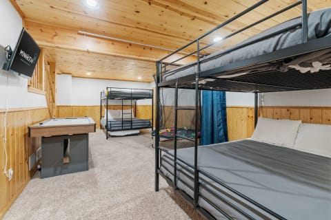 A cozy basement bedroom featuring bunk beds, a queen-sized bed, and an air hockey table.