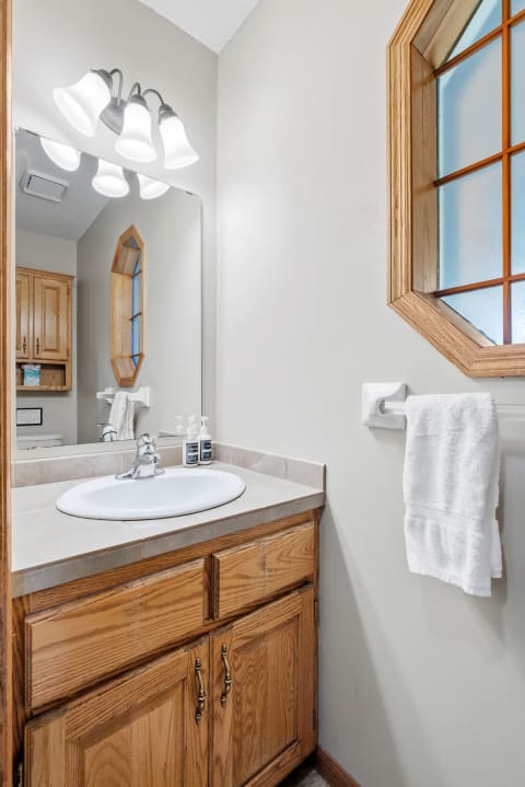 A well-lit bathroom featuring a white sink, wooden cabinets, and an octagonal window.