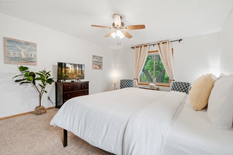 Cozy bedroom featuring a white bed, television, and natural light.
