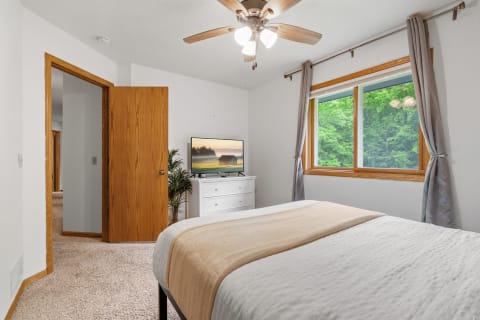 Cozy bedroom featuring a bed, a television, and a green view outside.