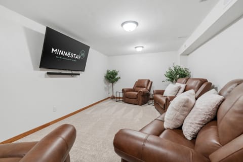 A cozy home theater featuring brown leather recliners, a mounted TV displaying the MINNESTAY logo, and soft lighting.