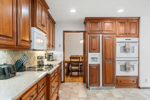 A cozy kitchen with wooden cabinets, a stove, and a dining area in the background.