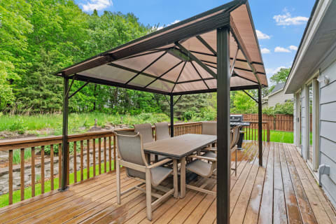 Outdoor patio with a gazebo, dining table, and lush trees in the background.