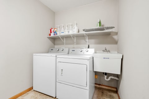 Laundry room featuring a washer, dryer, and utility sink against a gray wall.